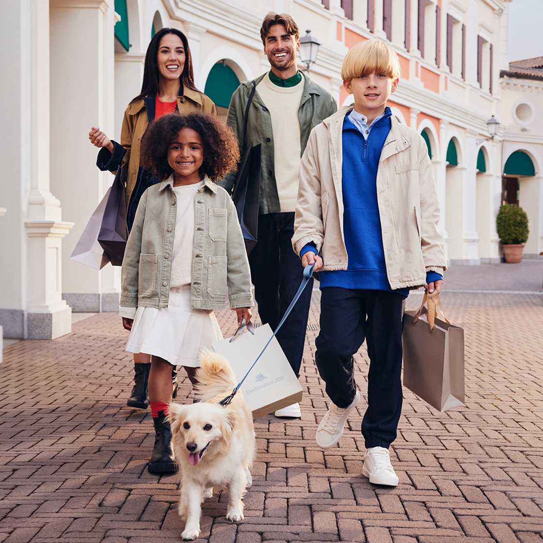 A happy family walking with shopping bags and their dog.